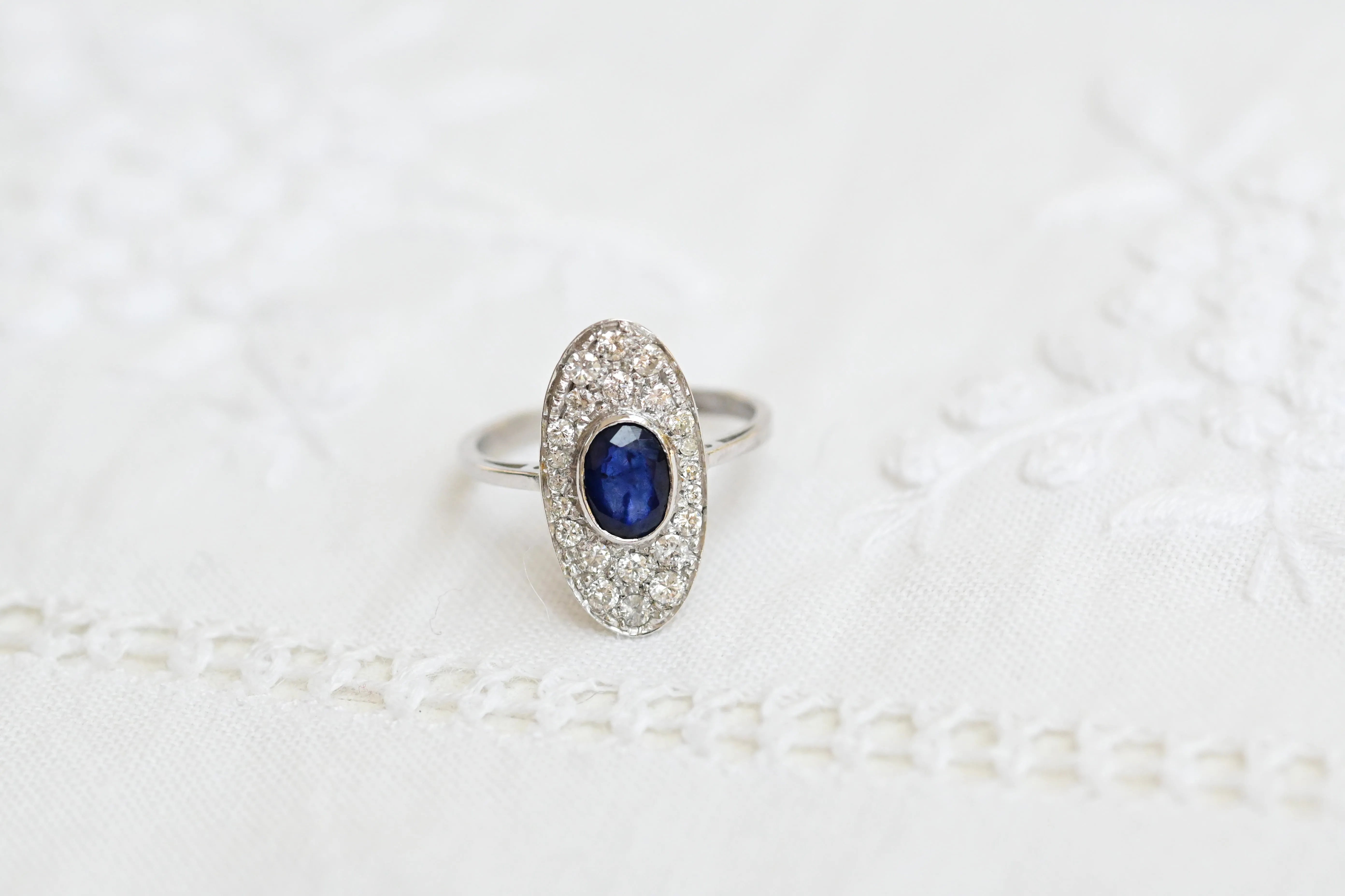 Anillo vintage con zafiro ovalado y diamantes, en oro blanco de 18K.