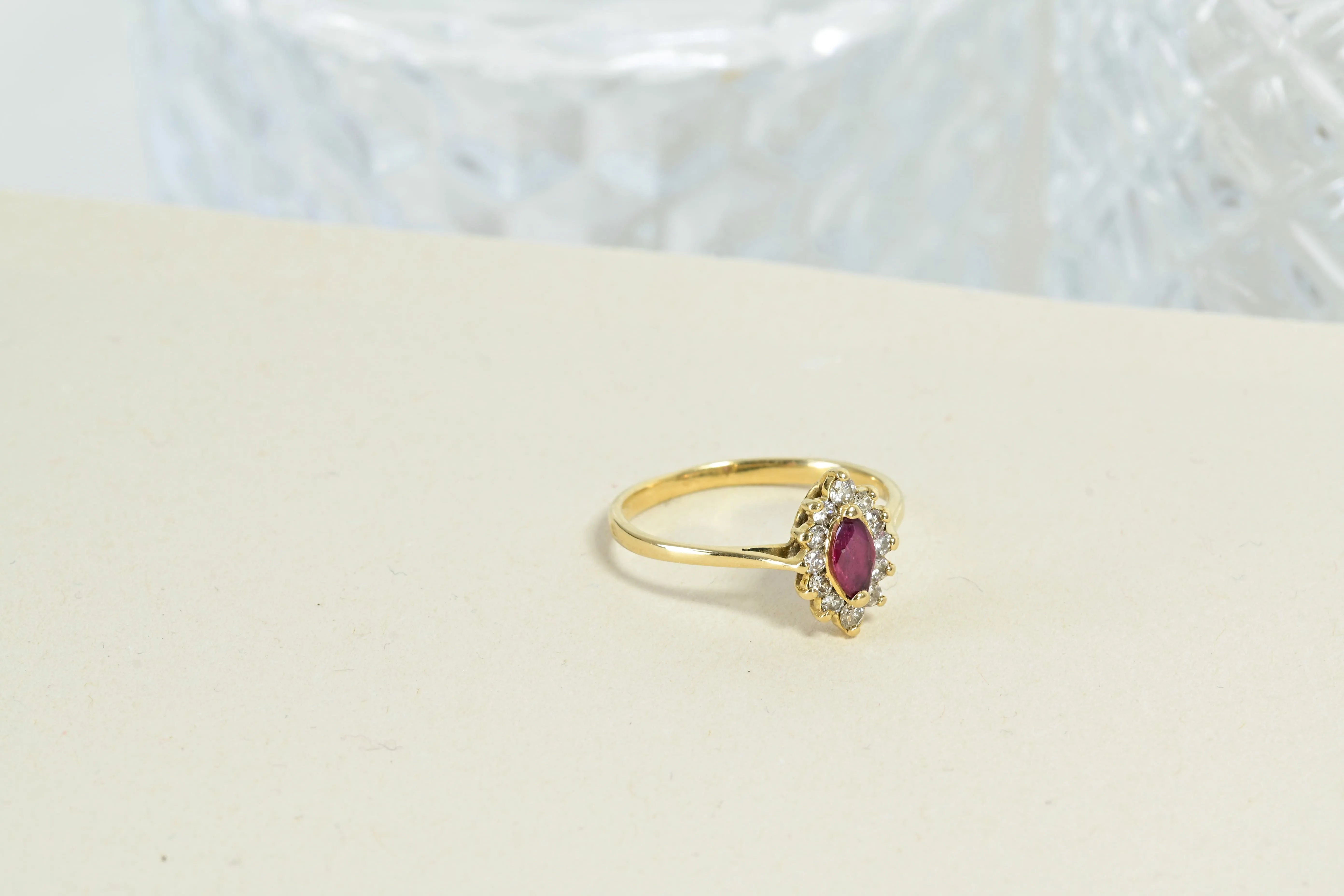 Anillo antiguo en forma de roseta con un rubí central en corte shuttle y 12 diamantes en oro amarillo de 18k, que muestra un diseño floral intrincado.