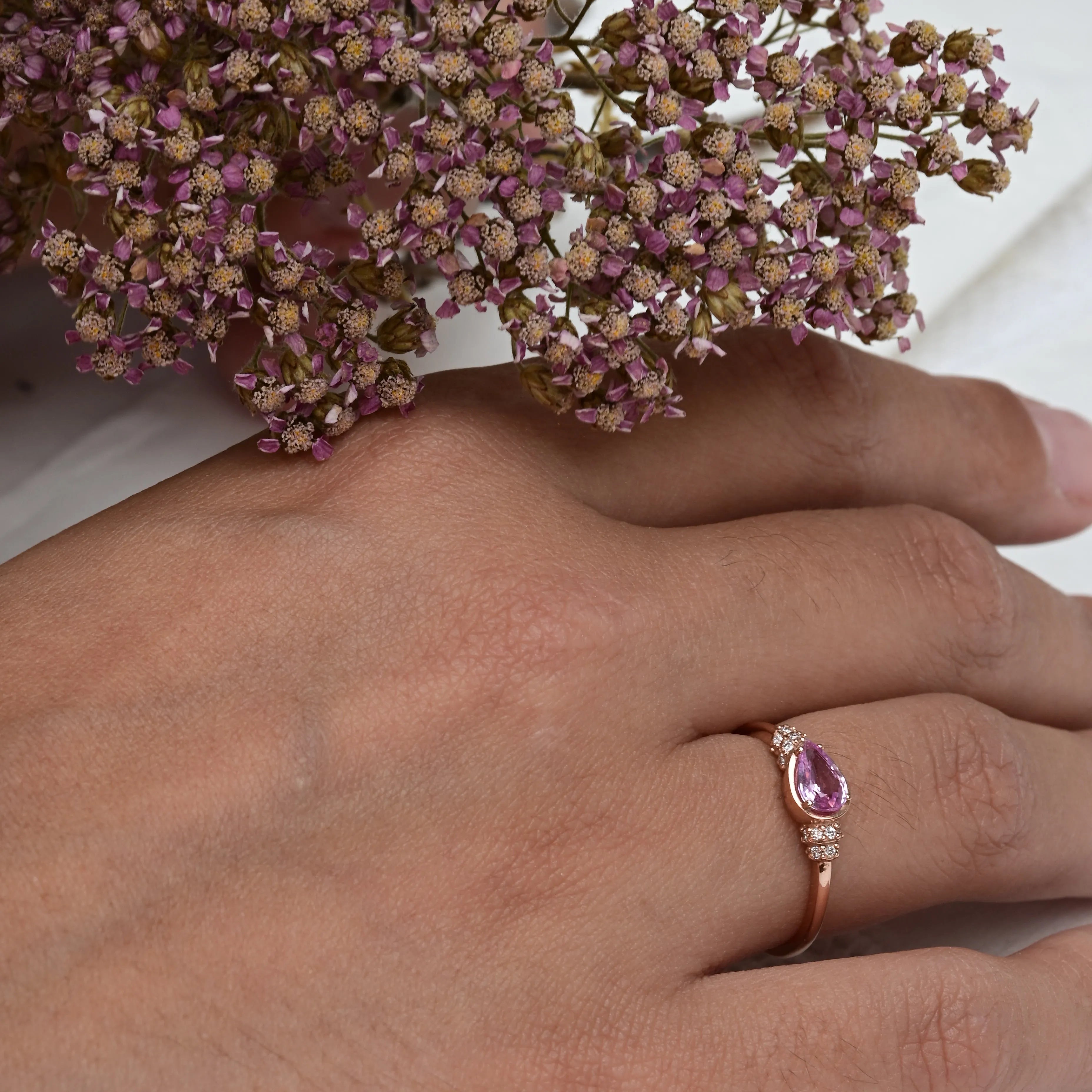 Vintage pink sapphire ring featuring a central pear-cut pink sapphire and 16 brilliant-cut diamonds, set in 14K rose gold.