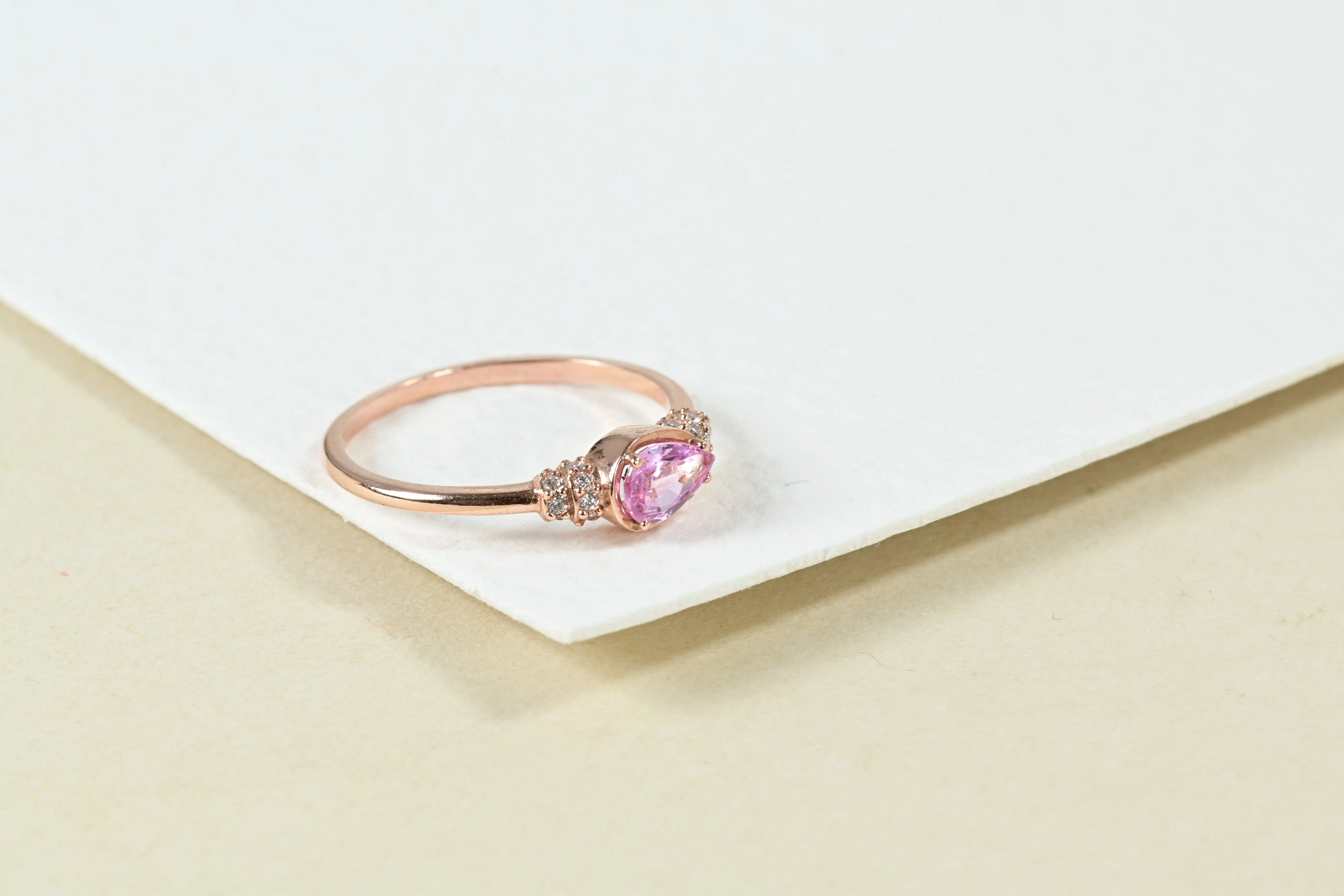 Anillo vintage con zafiro rosa en corte pera y 16 diamantes talla brillante, montado en oro rosa de 14K.