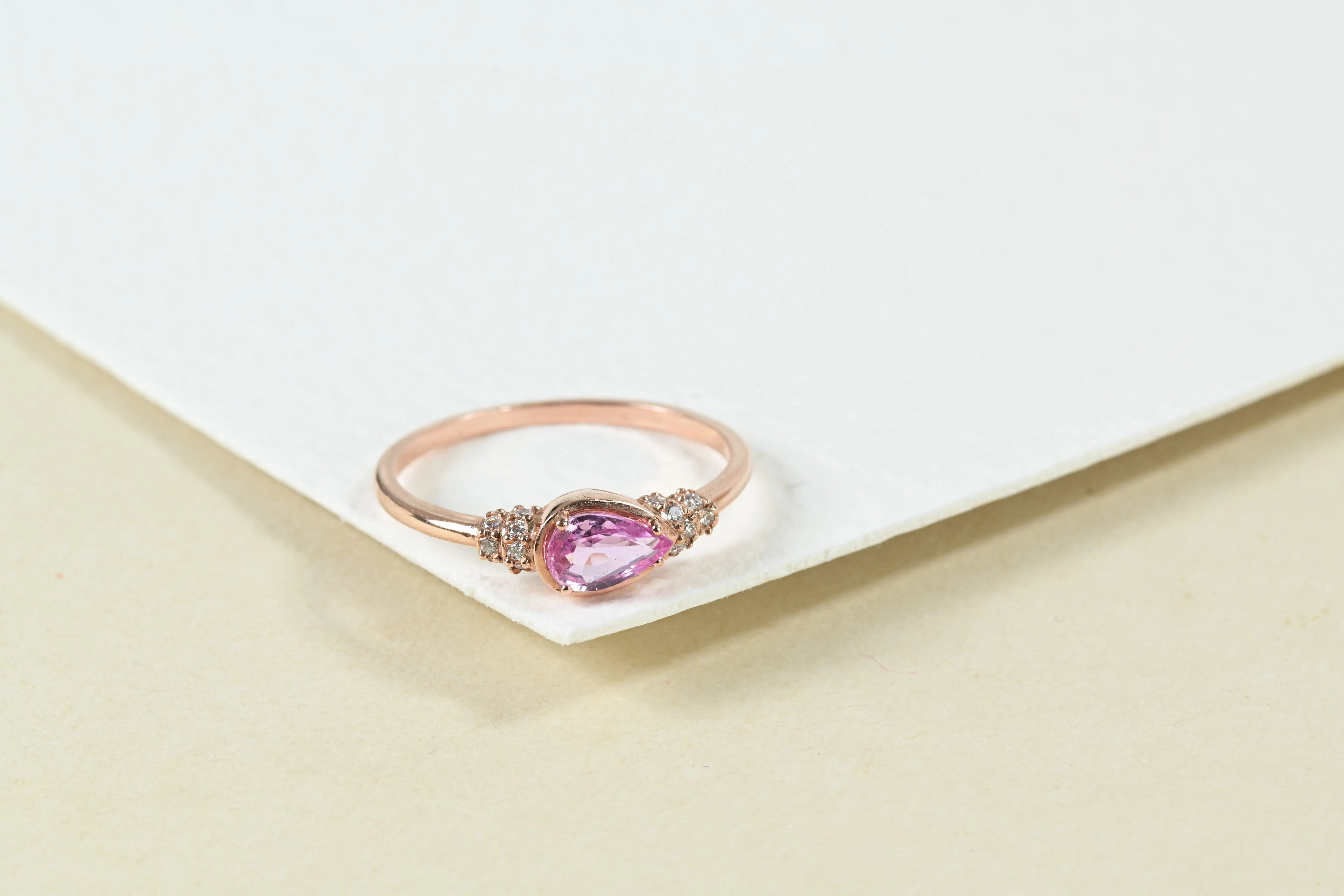 Vintage-Ring mit einem zentralen rosa Saphir im Tropfenschliff und 16 Brillanten, gefasst in 14K Roségold.