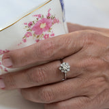 Flower-shaped engagement ring featuring one central round cut diamond and eight smaller brilliant cut diamonds in 18K white gold.