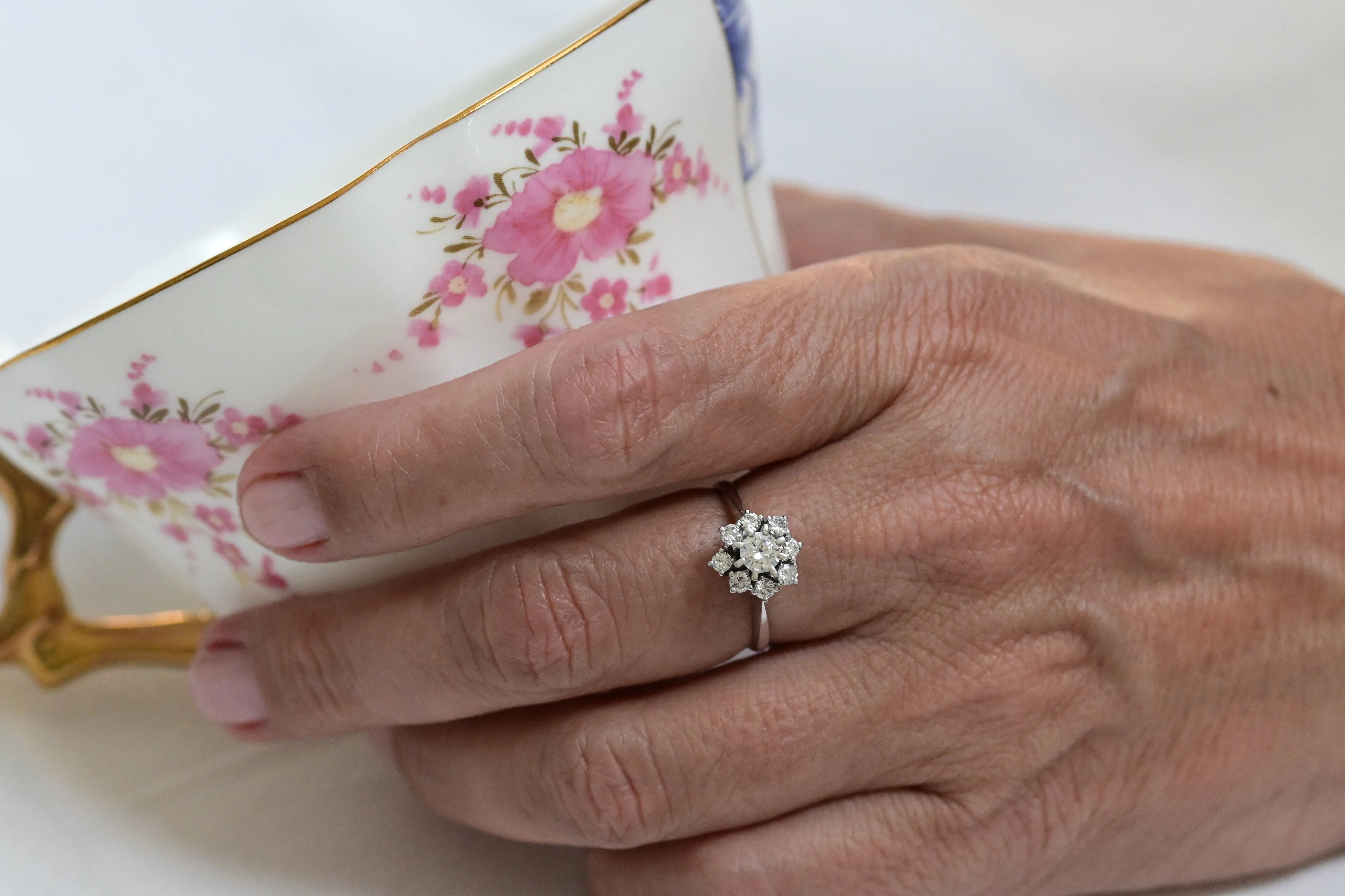 Flower-shaped engagement ring featuring one central round cut diamond and eight smaller brilliant cut diamonds in 18K white gold.