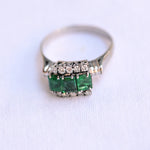 18K white gold vintage ring featuring 3 emeralds surrounded by 10 round cut diamonds.